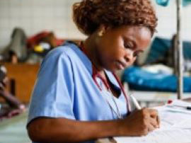    A female home health aide student in scrubs is taking notes on her patient